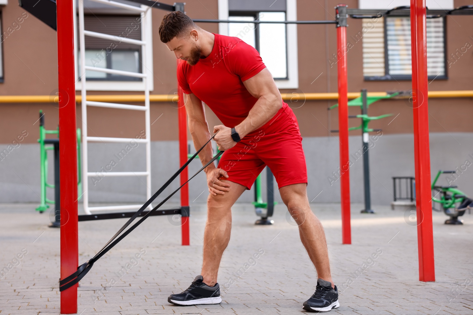 Photo of Muscular man doing exercise with elastic resistance band on sports ground