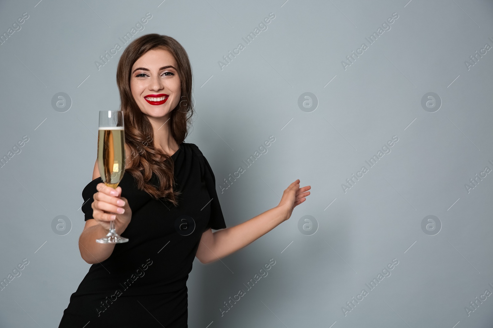 Photo of Happy woman with glass of champagne on grey background, space for text. Christmas party