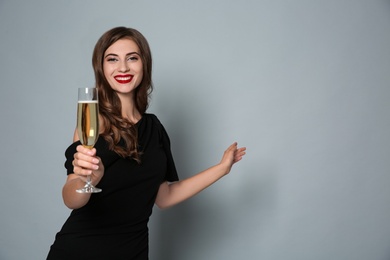 Photo of Happy woman with glass of champagne on grey background, space for text. Christmas party