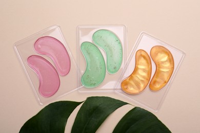 Under eye patches and tropical leaf on beige background, flat lay. Cosmetic product