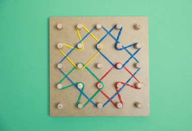 Photo of Wooden geoboard with rubber bands on green background, top view. Educational toy for motor skills development