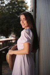 Beautiful young woman in stylish violet dress with straw hat outdoors