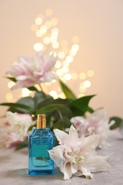 Photo of Bottle of perfume and beautiful lily flowers on table against beige background with blurred lights, closeup