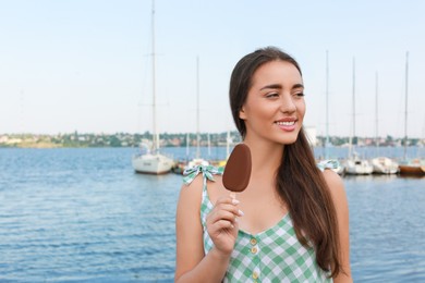 Photo of Beautiful young woman holding ice cream glazed in chocolate near river, space for text