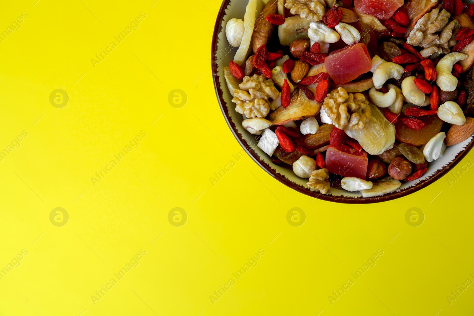 Photo of Bowl with mixed dried fruits and nuts on yellow background, top view. Space for text