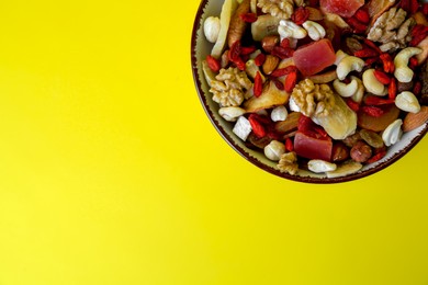 Photo of Bowl with mixed dried fruits and nuts on yellow background, top view. Space for text