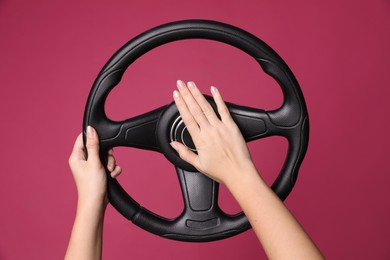 Photo of Woman holding steering wheel on crimson background, closeup