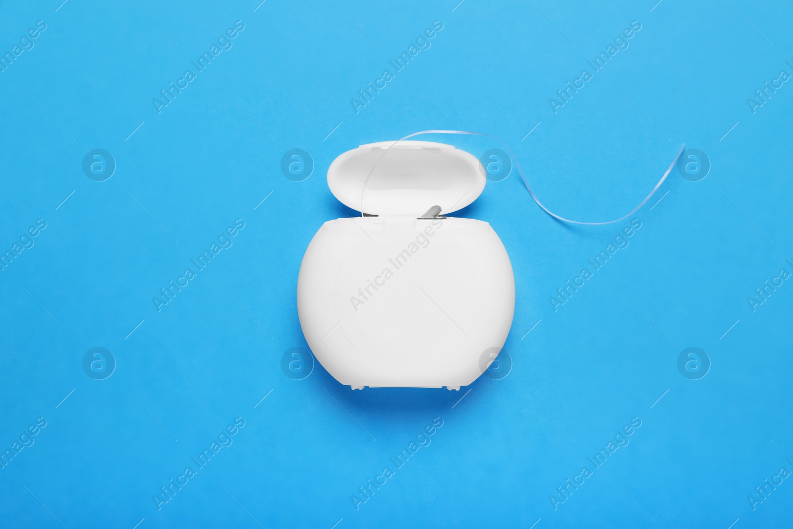 Photo of Container with dental floss on light blue background, top view