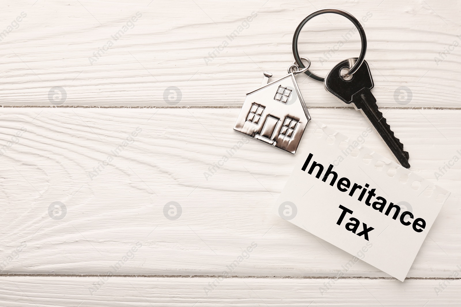 Photo of Inheritance Tax. Note and key with metallic key chain in shape of house on white wooden table, flat lay. Space for text