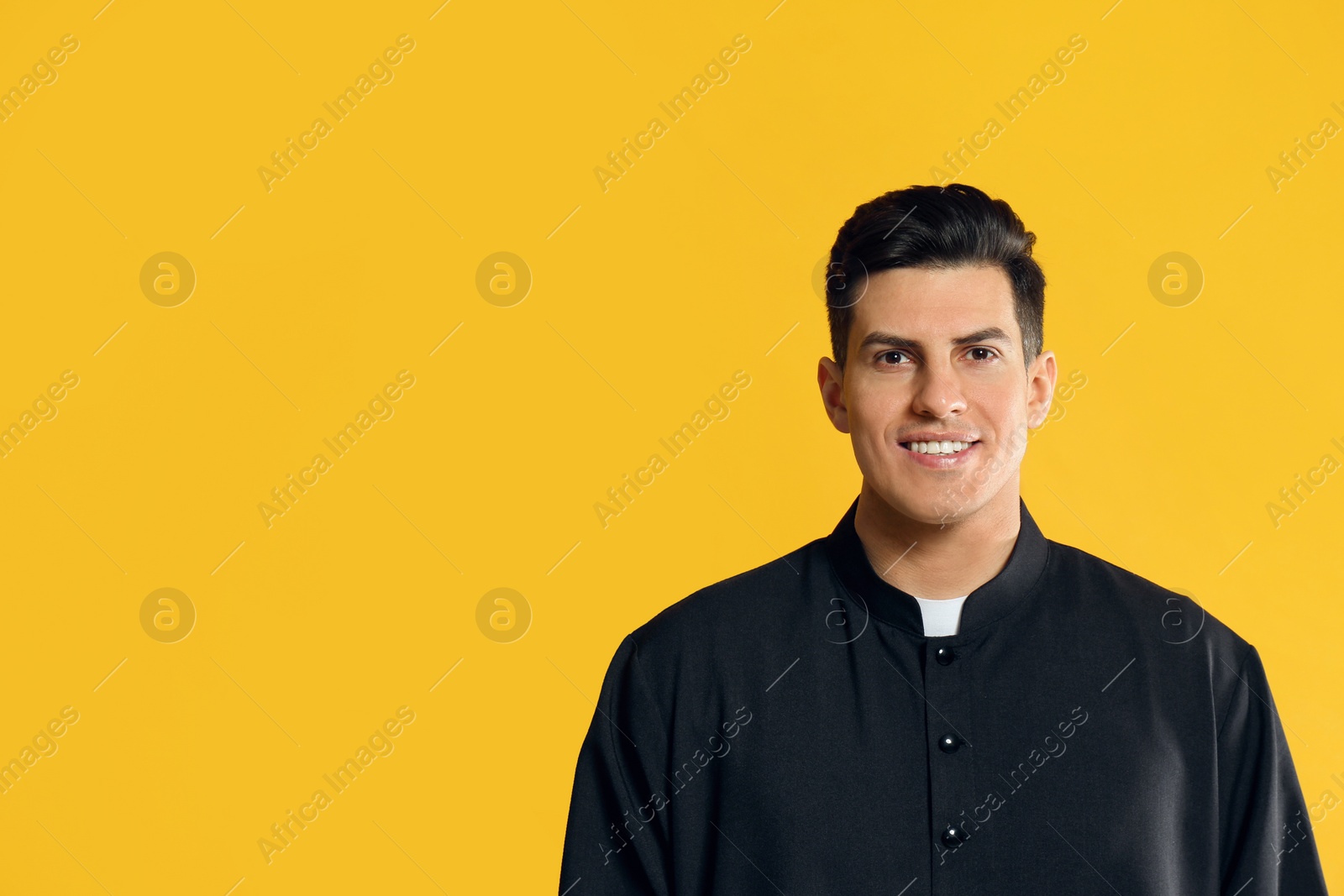 Photo of Priest wearing cassock with clerical collar on yellow background. Space for text