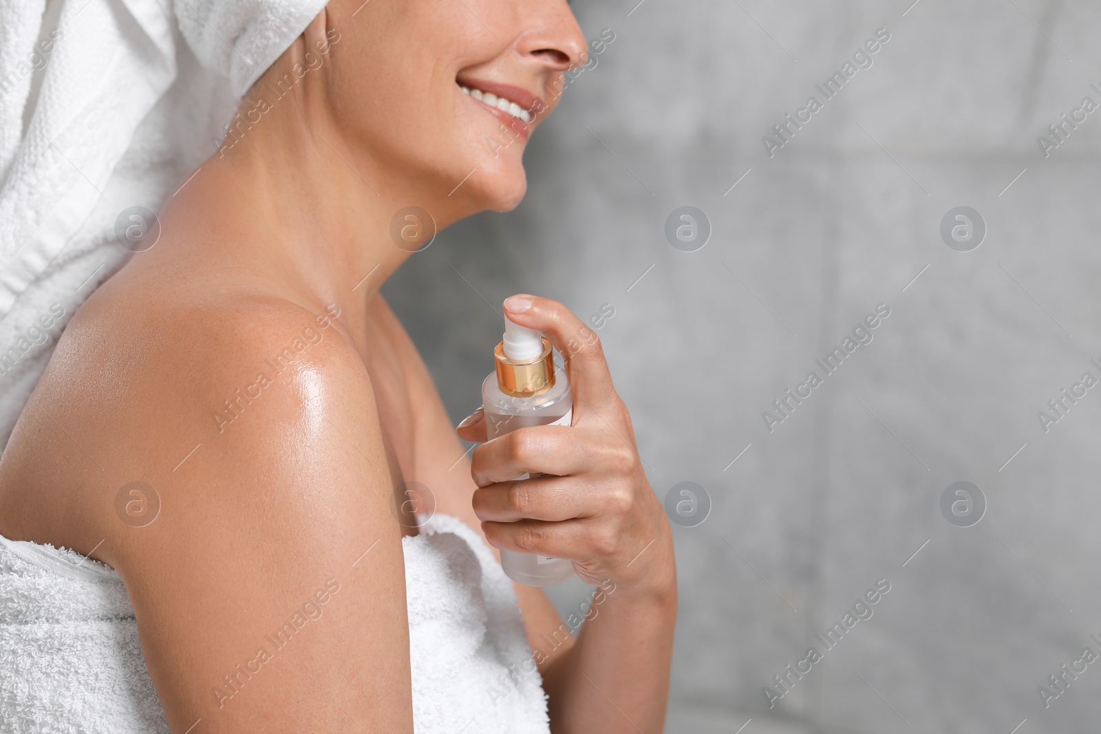 Photo of Happy woman applying body oil onto shoulder near grey wall, closeup. Space for text