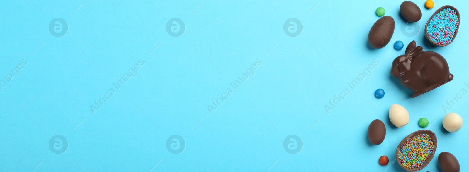 Photo of Flat lay composition with chocolate Easter bunny, eggs and candies on light blue background. Space for text