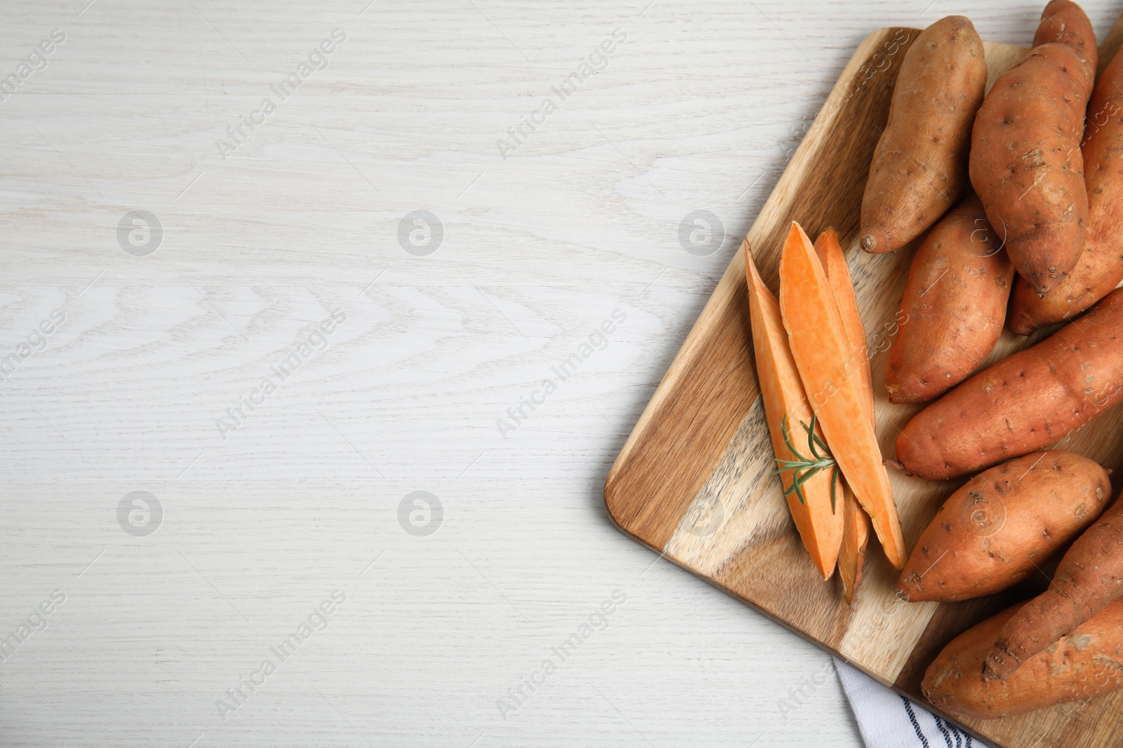 Photo of Board with cut and whole sweet potatoes on white wooden table, flat lay. Space for text