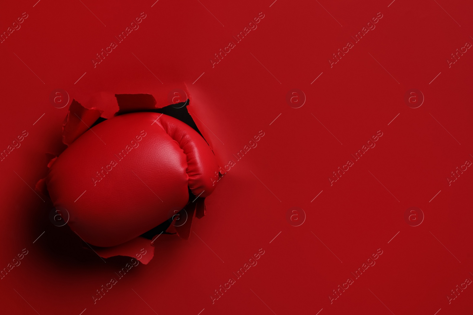 Photo of Man breaking through red paper with boxing glove, closeup. Space for text