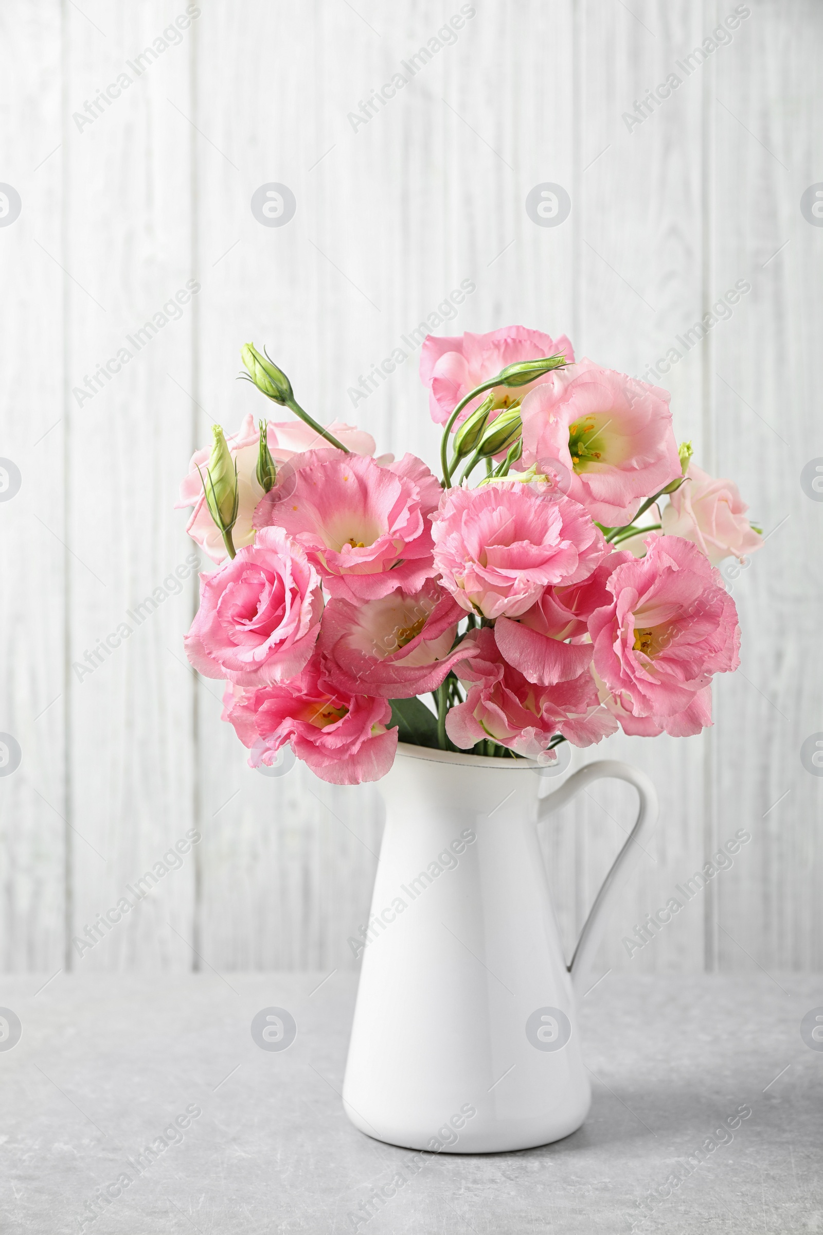 Photo of Eustoma flowers in vase on table near white wall