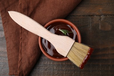 Photo of Marinade in bowl and basting brush on wooden table, top view