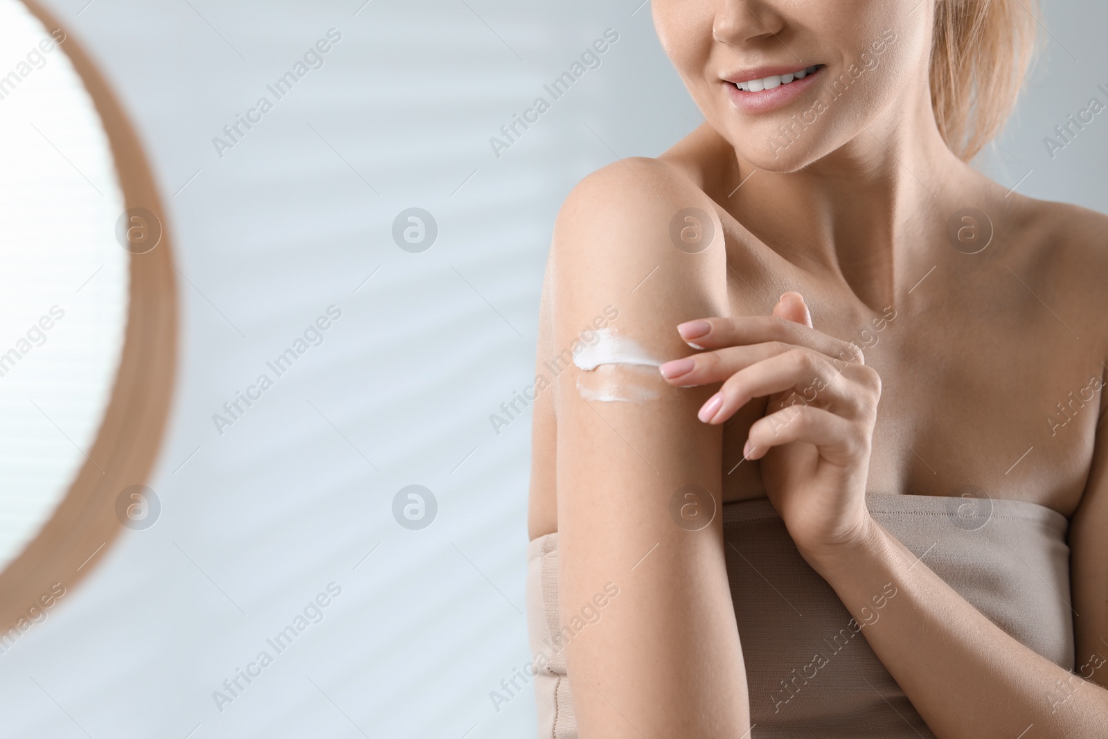 Photo of Woman applying body cream onto arm indoors, closeup. Space for text