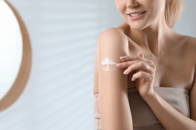 Photo of Woman applying body cream onto arm indoors, closeup. Space for text