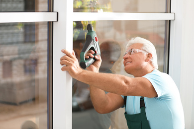 Photo of Mature construction worker repairing plastic window with electric screwdriver indoors