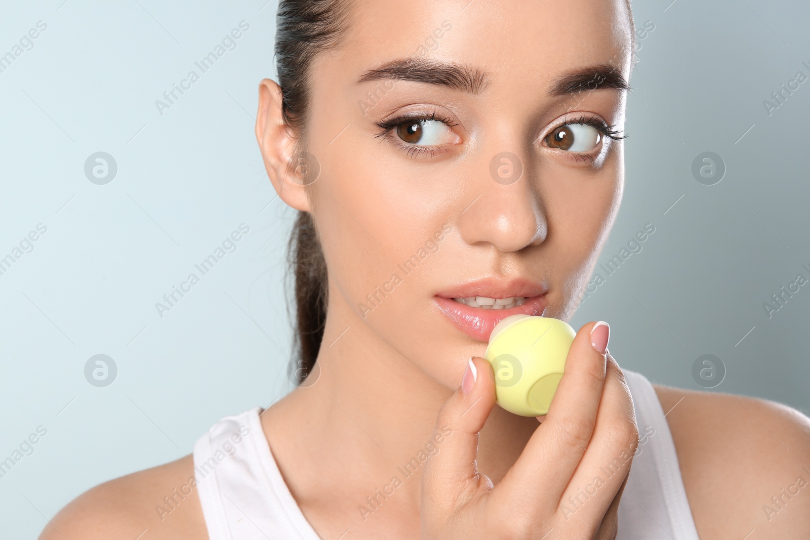 Photo of Young woman applying balm on her lips against color background