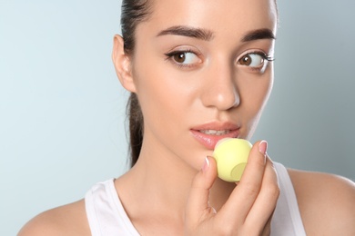 Photo of Young woman applying balm on her lips against color background