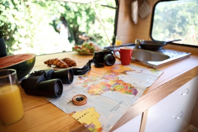 Photo of World map and travel accessories on wooden table in motorhome. Summer trip