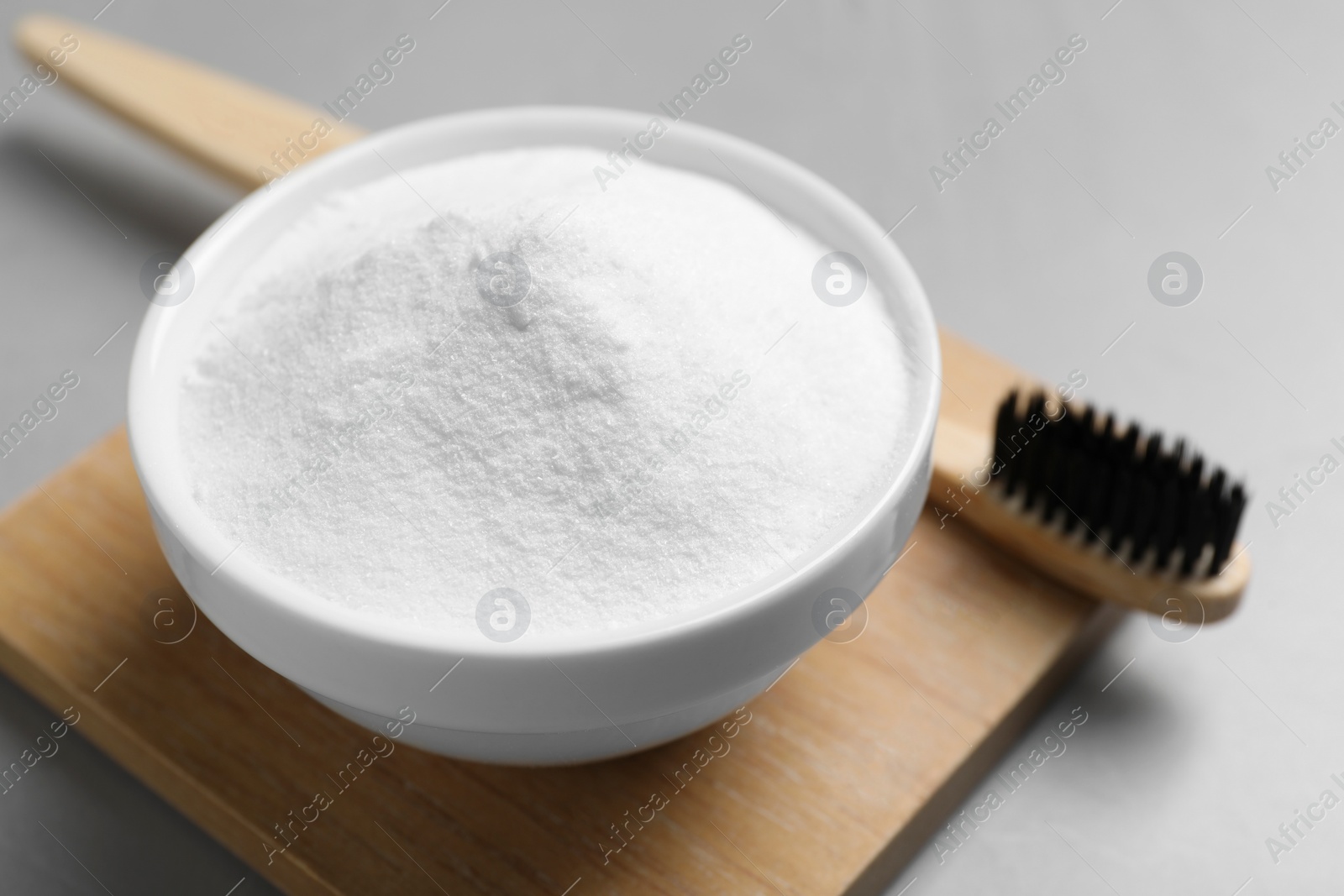 Photo of Bamboo toothbrush and bowl of baking soda on grey table, closeup. Space for text