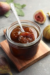 Photo of Jar of tasty sweet fig jam on grey table