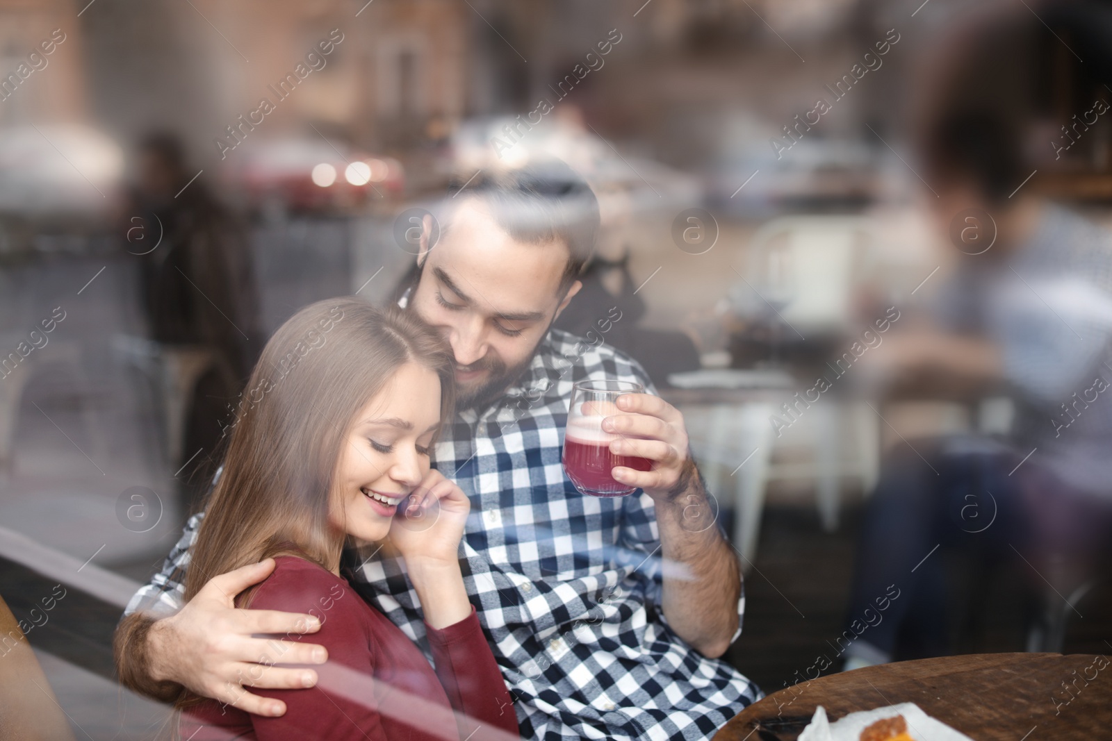 Photo of Lovely young couple spending time together in cafe, view from outdoors through window