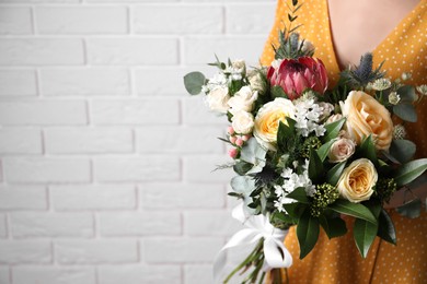 Photo of Woman with bouquet of beautiful roses near white brick wall, closeup. Space for text