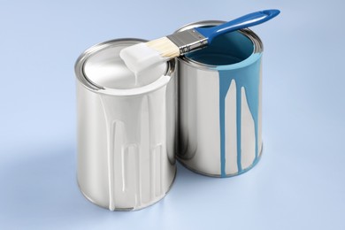 Photo of Cans of paints and brush on light blue background