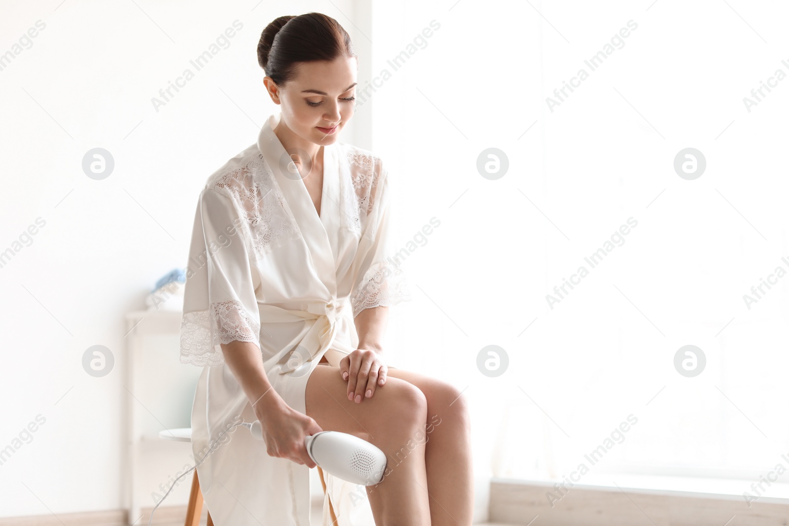 Photo of Beautiful young woman removing hair with modern laser epilator at home