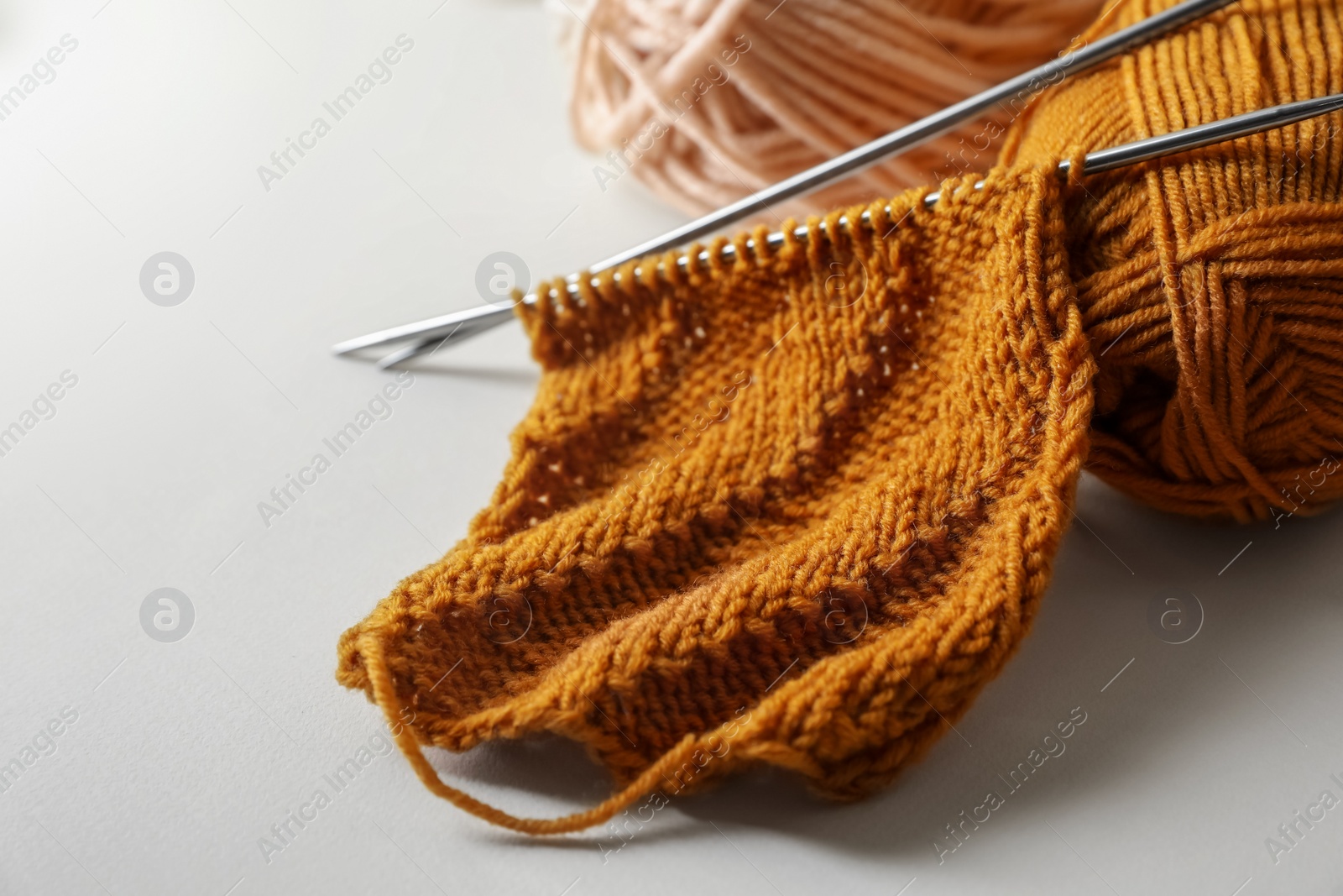 Photo of Soft orange knitting, colorful yarns and metal needles on beige background, closeup