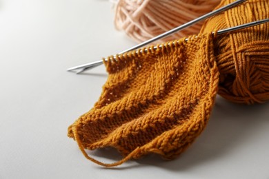 Photo of Soft orange knitting, colorful yarns and metal needles on beige background, closeup