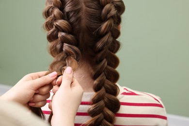 Photo of Professional stylist braiding woman's hair on olive background, closeup