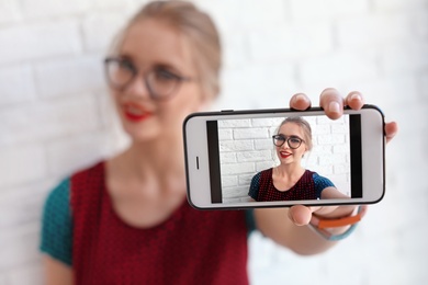 Attractive young woman taking selfie near brick wall, closeup