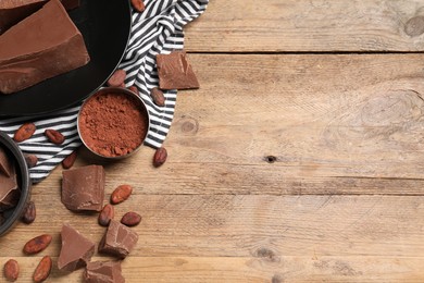 Photo of Pieces of tasty milk chocolate, cocoa beans and powder on wooden table, flat lay. Space for text