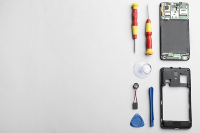 Disassembled mobile phone and repair tools on light background, flat lay
