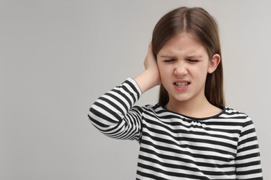 Photo of Hearing problem. Little girl suffering from ear pain on grey background, space for text