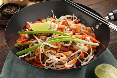 Photo of Shrimp stir fry with noodles and vegetables in wok on wooden table