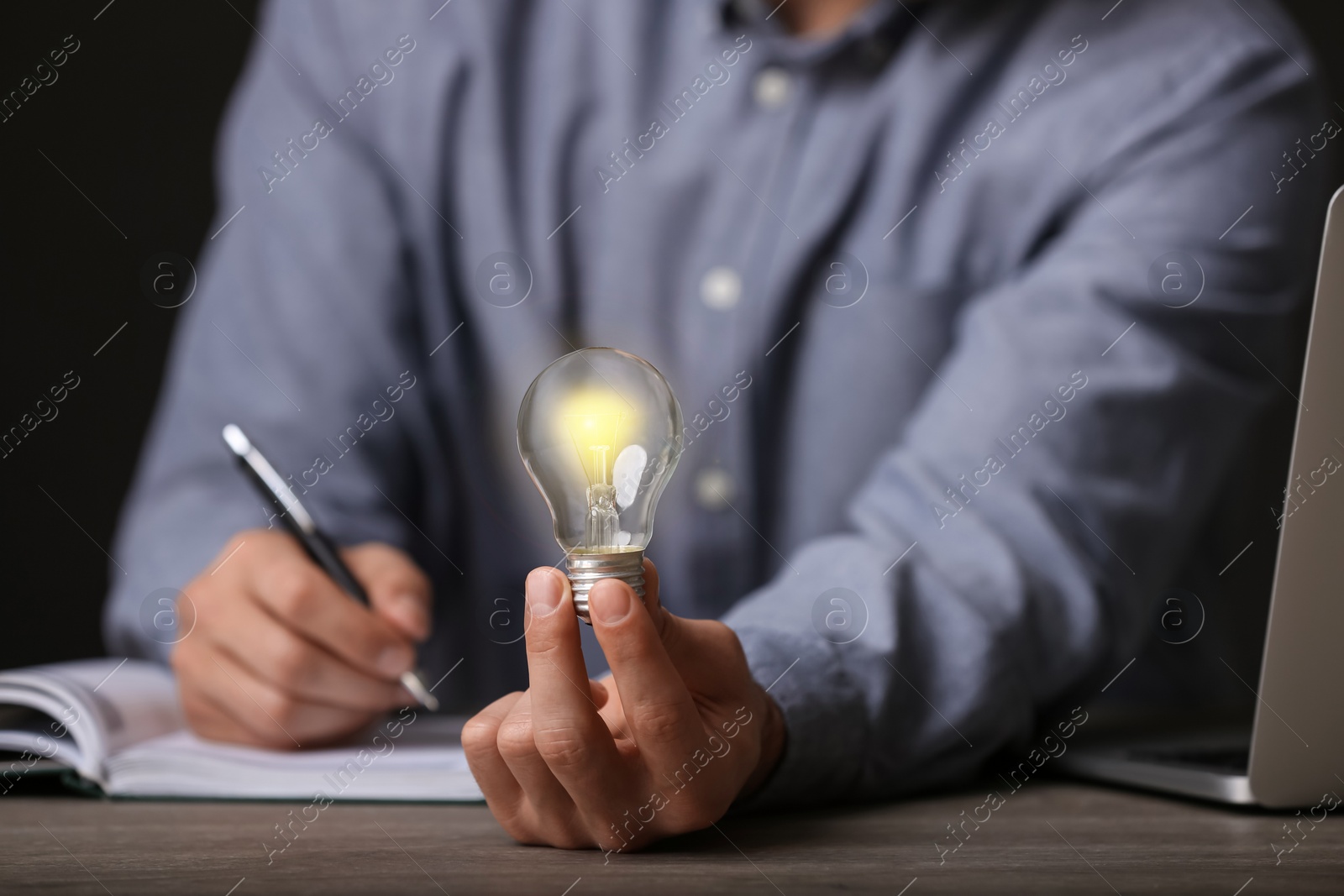 Photo of Glow up your ideas. Closeup view of man holding light bulb while working at wooden desk