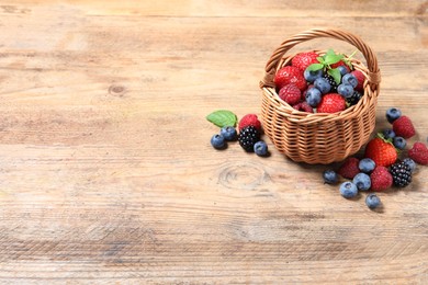 Photo of Wicker basket with many different fresh ripe berries on wooden table, space for text