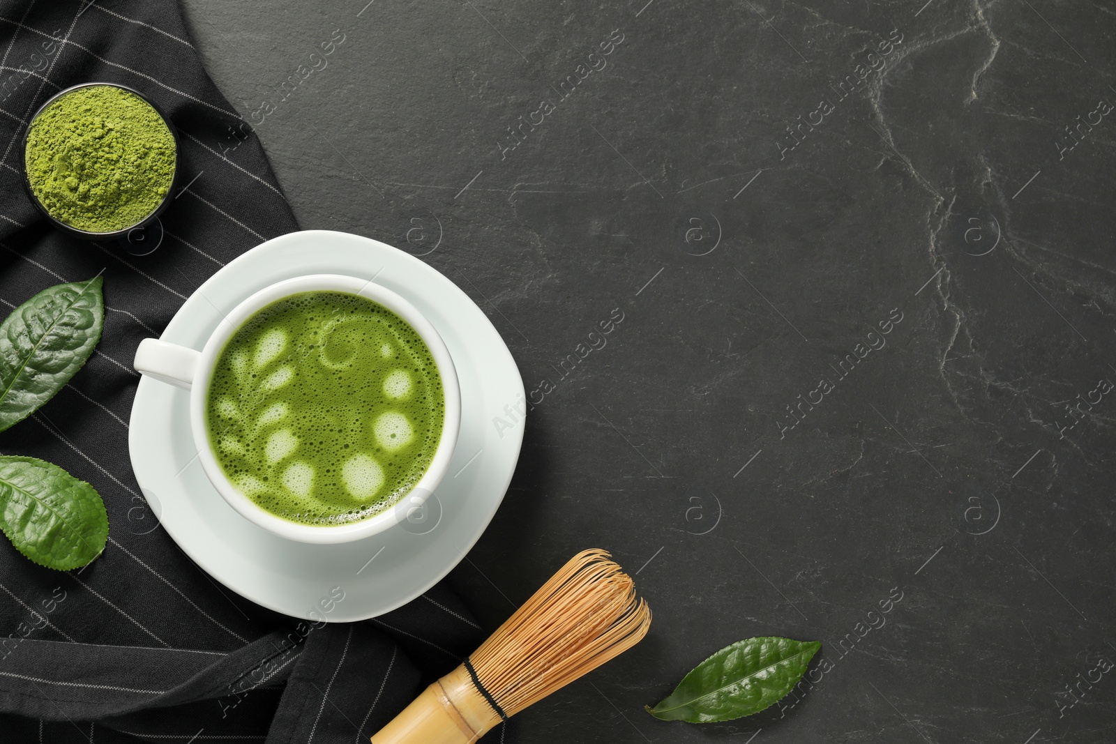 Photo of Delicious matcha latte, powder, leaves and whisk on dark textured table, flat lay. Space for text