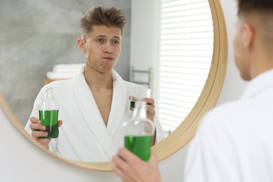 Photo of Young man using mouthwash near mirror in bathroom