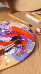 Artist's palette with mixed paints and brushes on wooden table, closeup