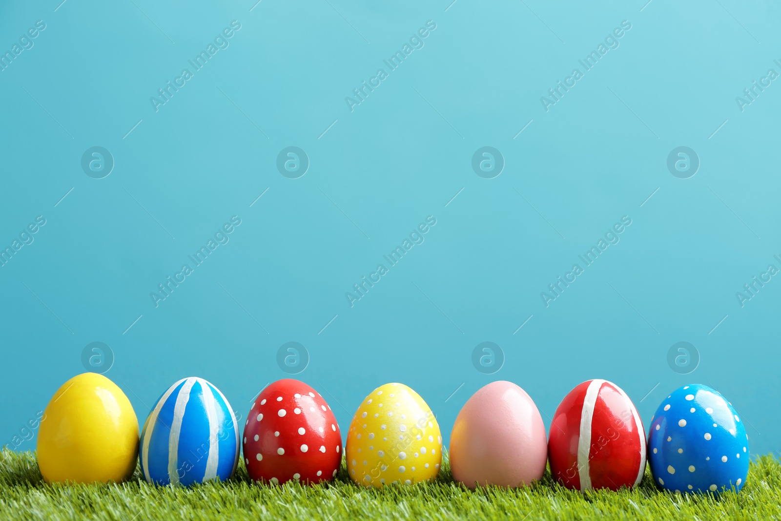 Photo of Painted Easter eggs on green grass against color background, space for text