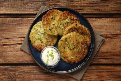Photo of Delicious zucchini fritters with sour cream served on wooden table, top view