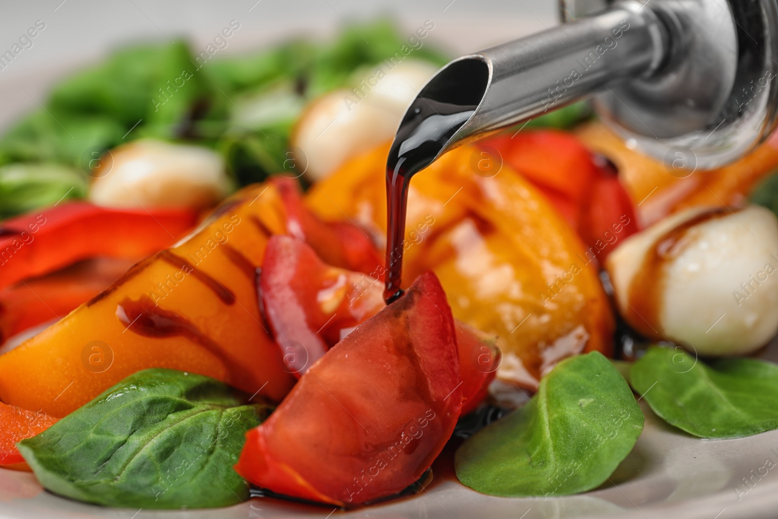 Photo of Pouring balsamic vinegar onto vegetable salad, closeup