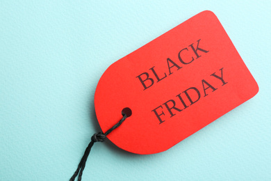 Photo of Red tag with words BLACK FRIDAY on turquoise background, top view