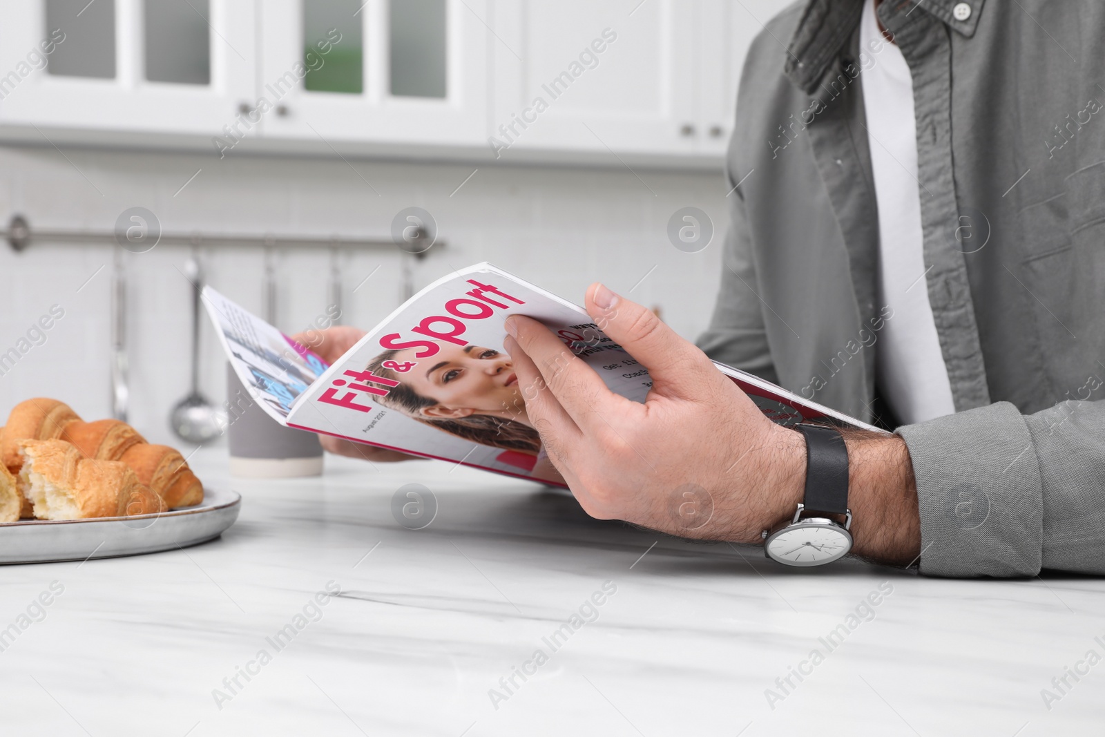 Photo of Man reading magazine at white marble table in kitchen, closeup